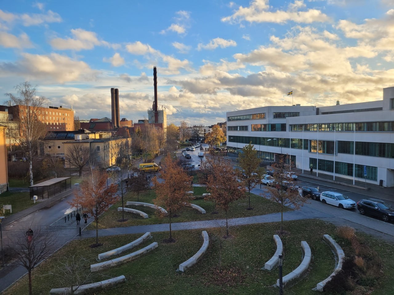 Autumn campus: curved benches, red foliage and a building flying the Swedish flag