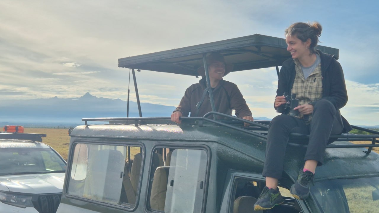 Riding on safari jeep pop-top roof looking at distant mountains